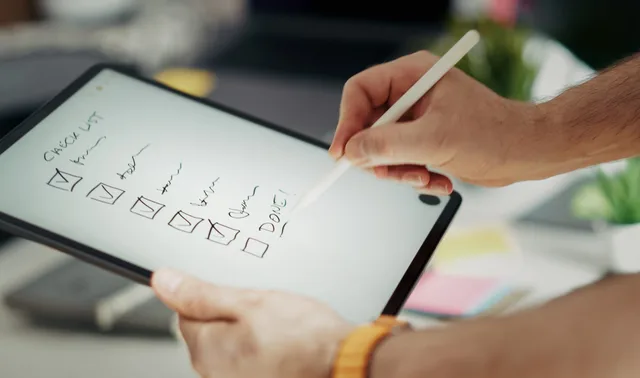 Close-up of a hand writing on a digital checklist using a stylus on a tablet, enhancing productivity. Small business CRM commercial opportunities to test